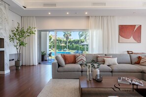 A modern living room with a grey sofa, a coffee table, and a view of a pool. - Luxury 5BR Villa Benalmádena | Pool & Jacuzzi REF073 (Benalmádena)