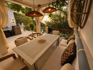 Een terras met een tafel, stoelen en hangende rieten lampen.