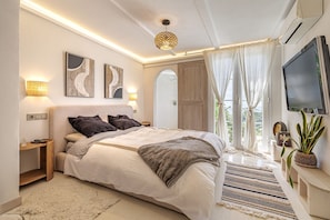 A modern bedroom with a large bed, bedside lamps, a TV, and a view of the outdoors.
