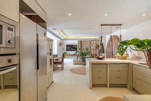 Une cuisine moderne dotée d’appareils électroménagers intégrés, un coin repas avec une table ronde et un espace de vie agrémenté d’un téléviseur et de plantes.