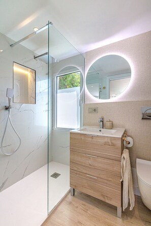 Une salle de bain moderne avec une douche à parois de verre, un meuble-lavabo en bois, un miroir rond et un lavabo blanc.