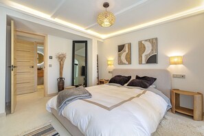 Een slaapkamer met een bed, nachtkastjes, een spiegel, kunstwerken en een deur naar een badkamer.
