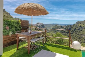 Une table en bois surmontée d’un parasol en chaume, entourée d’une végétation luxuriante et offrant une vue pittoresque.