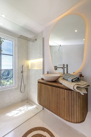 Een moderne badkamer met een houten wastafelmeubel, een grote spiegel, een waskom en een douche.
