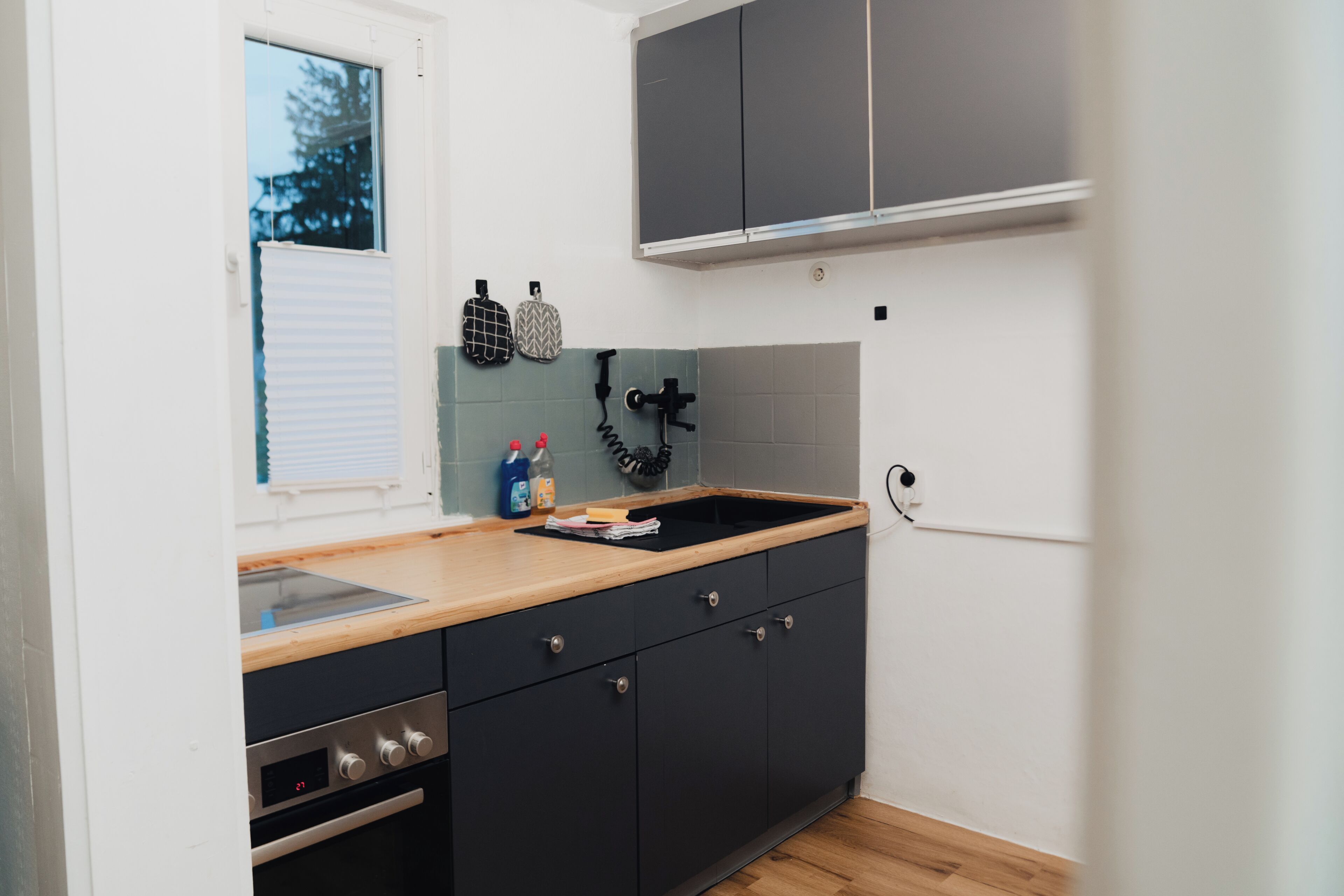 Eine Küche mit Holzarbeitsplatte, schwarzen Schränken, einem eingebauten Backofen und einem Fenster mit Jalousien.