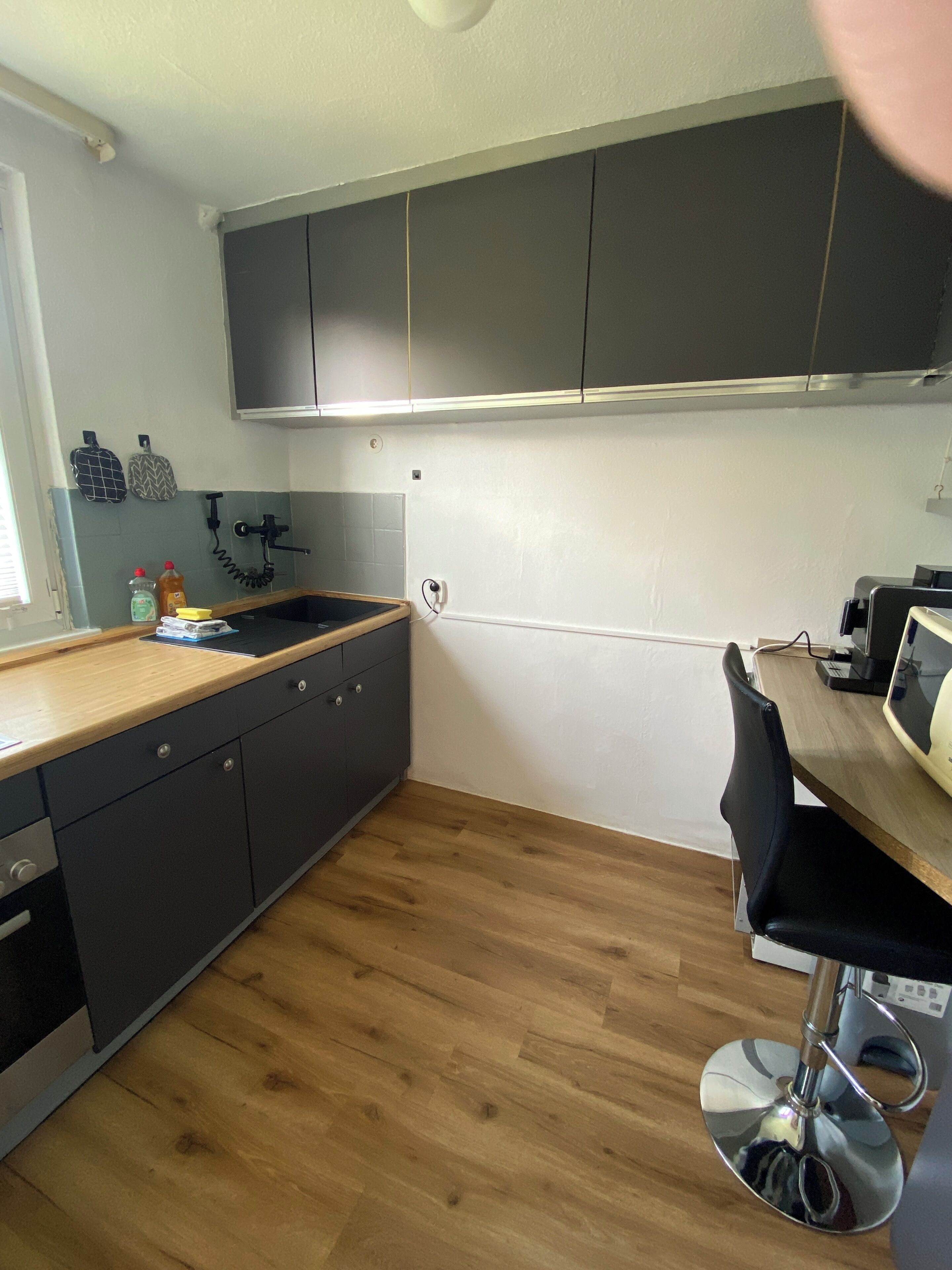 A kitchen with dark cabinets, a wooden countertop, a sink, and a chair.