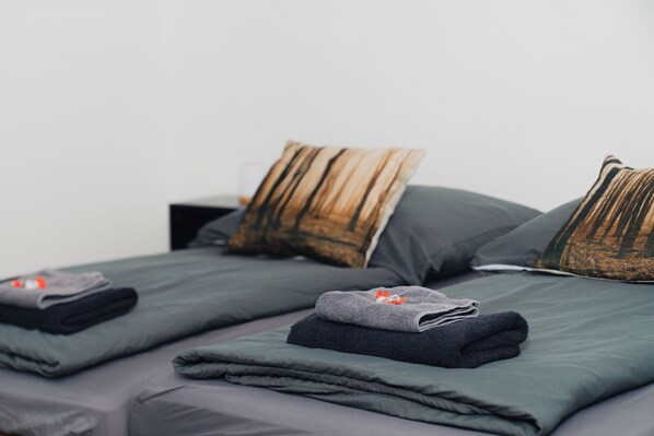 Ein ordentlich bezogenes Bett mit grauer Bettwäsche und gestreiften Kissen, ein gefaltetes Handtuch und ein kleiner Nachttisch.