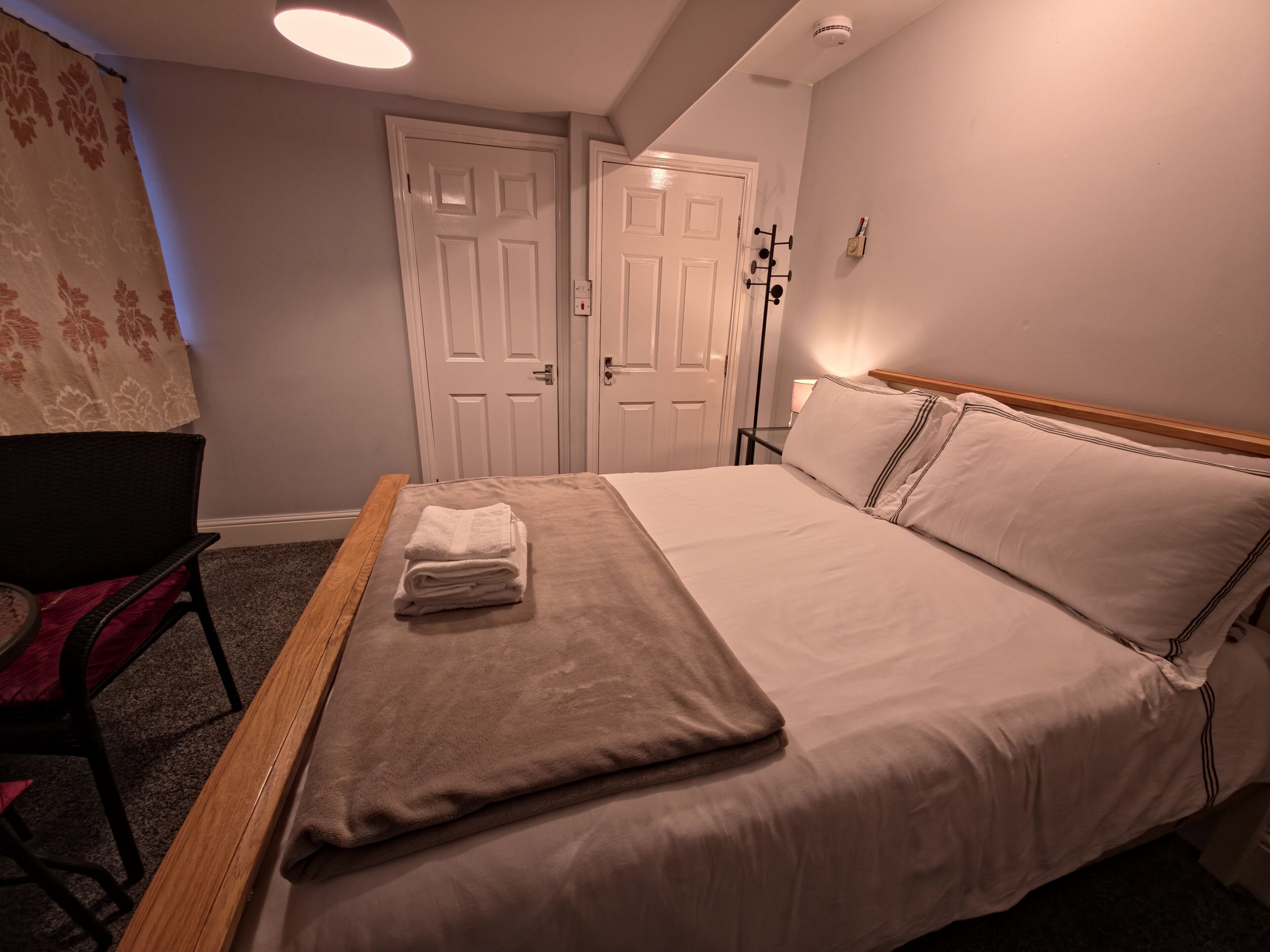 Hotellihuone, jossa on sänky, tuoli, työpöytä ja kaksi ovea.