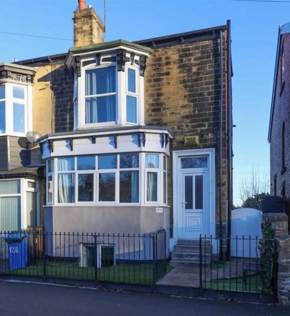 A corner house with a bay window, a white door, and a brick wall.