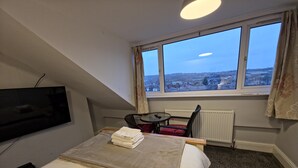 Ein Hotelzimmer mit Bett, Fernseher, Fenster mit Blick, Sessel und Tisch.
