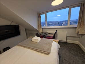 A hotel room with a bed, a TV, a window with a view, a chair, and a table.