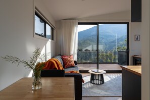 Un salon moderne avec un canapé, une table basse, une vue sur les montagnes et un balcon doté d’une balustrade.