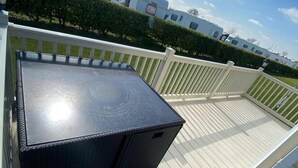 A deck with a black table, white railing, and a hedge in the background.