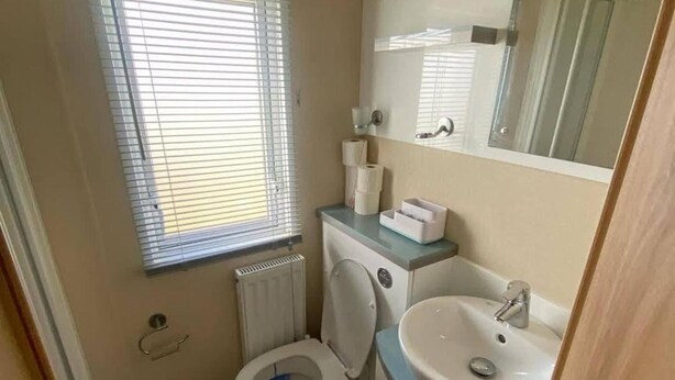 Een compacte badkamer met toilet, wastafel en een raam met zonwering.