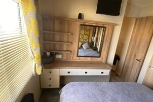 Quarto com penteadeira de madeira, espelho, cama e televisão fixada na parede.