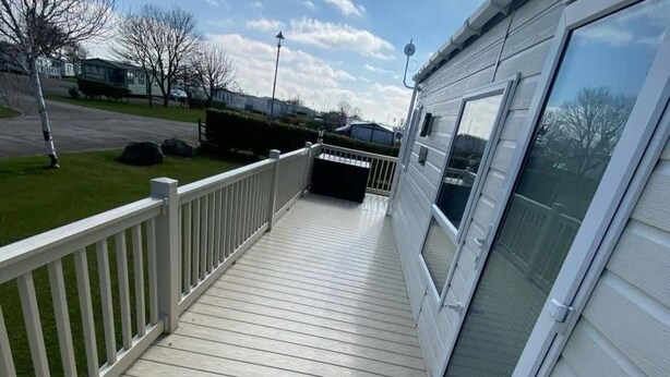 A wooden deck with a white railing, a covered porch, and a large window on the right side.