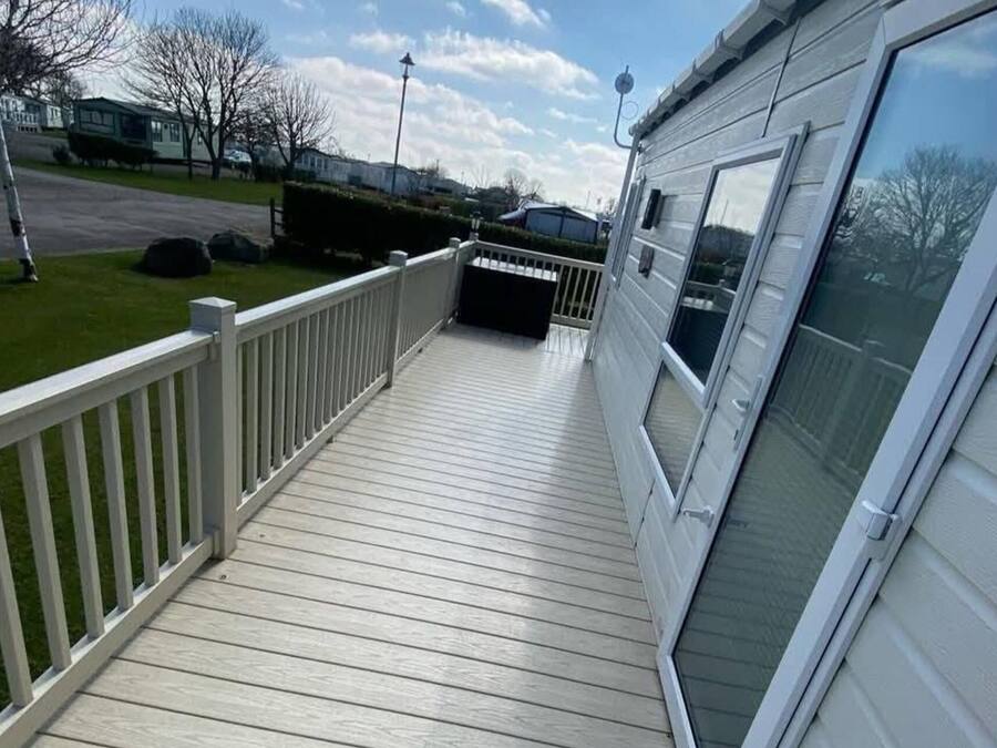 A wooden deck with a white railing, a covered porch, and a large window on the right side.