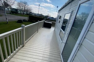Um deck de madeira com guarda-corpo branco, um alpendre coberto e uma janela grande no lado direito.