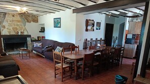 Un salon avec une cheminée, un coin repas avec des chaises et une table en bois, et une cuisine équipée de placards et d’un four à micro-ondes.