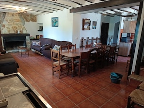A living room with a fireplace, a dining area with wooden chairs and a table, and a kitchen area with cabinets and a microwave.
