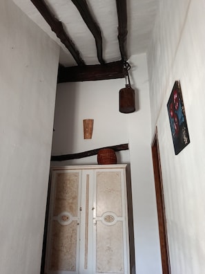 A hallway with a wooden ceiling, a white wall, a door with decorative panels, and a hanging light fixture.