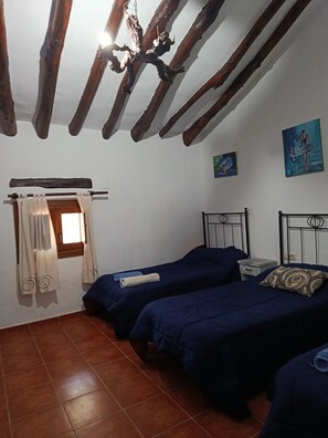 A room with two beds, a wooden ceiling, a window with curtains, and two paintings on the wall.