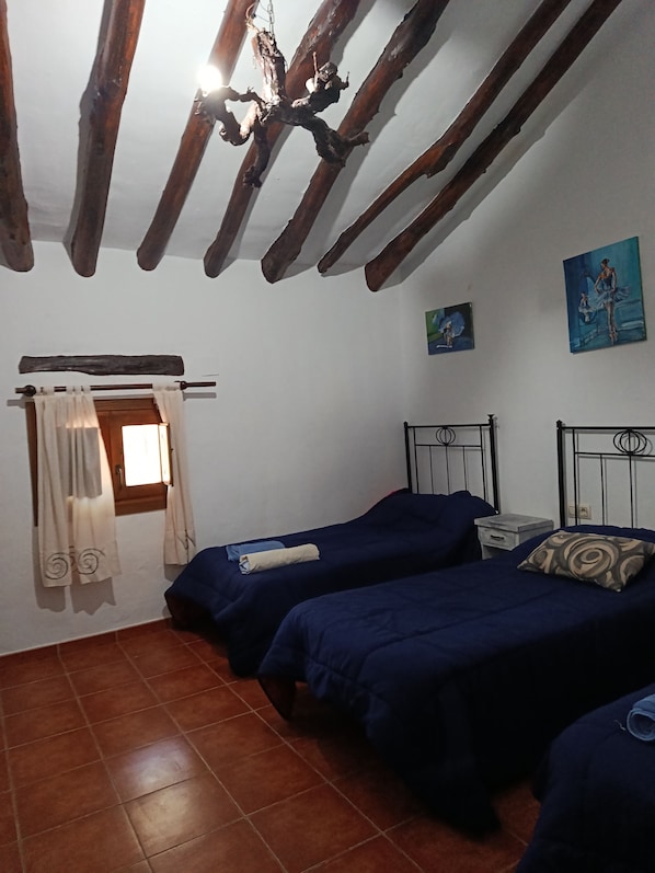 A room with two beds, a wooden ceiling, a window with curtains, and two paintings on the wall.