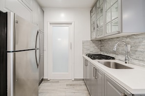 A narrow kitchen with white cabinets, a stainless steel refrigerator, a tiled backsplash, and a sink. - South Beach Ocean Drive Villa | Pool | Oceanfront (Miami)
