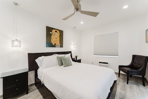 A bedroom with a bed, a ceiling fan, a painting, a window with blinds, and a chair. - South Beach Ocean Drive Villa | Pool | Oceanfront (Miami)