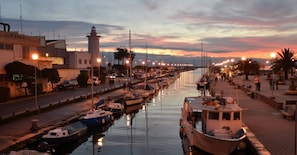 A marina with boats docked along the water, a lighthouse, and a street with buildings and palm trees. - Appartamento DUE Camere (Camaiore)