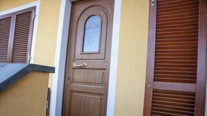 A wooden door with a small window, a metal handle, and a sliding door with horizontal slats. - Appartamento DUE Camere (Camaiore)