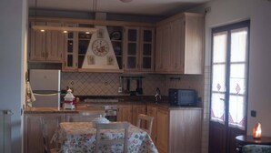 A kitchen with wooden cabinets, a dining table with chairs, a refrigerator, and a microwave. - Appartamento DUE Camere (Camaiore)