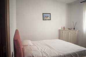 Una camera da letto con un letto, un quadro appeso al muro, un mobiletto con una ciotola e una finestra con tende.