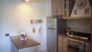 A kitchen with wooden cabinets, a stainless steel refrigerator, a gas stove, and a clock on the wall. - Appartamento DUE Camere (Camaiore)