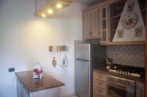 A kitchen with wooden cabinets, a stainless steel refrigerator, a gas stove, and a clock on the wall. - Appartamento DUE Camere (Camaiore)