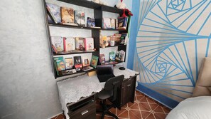 Ein Zimmer mit Schreibtisch, Regalen mit Büchern, einem Laptop und einer Wand mit Muster.