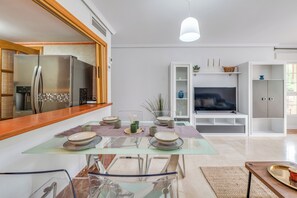 A modern kitchen with a built-in refrigerator, a dining table set with plates and bowls, a TV in the living area, and a bookshelf. - LXR Coloso, 2-bedroom apartment with an ocean view. (Benalmádena)