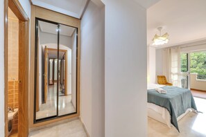A bedroom with a bed, a window with curtains, a yellow chair, and a hallway with a mirror. - LXR Coloso, 2-bedroom apartment with an ocean view. (Benalmádena)