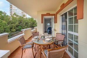 A balcony with a dining table set for four, surrounded by wicker chairs, a view of trees, and a building in the background. - LXR Coloso, 2-bedroom apartment with an ocean view. (Benalmádena)