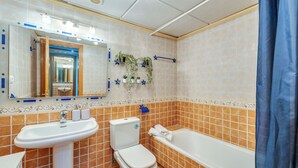 A bathroom with a sink, toilet, and bathtub, tiled in orange and white, with a mirror and decorative plants. - LXR Coloso, 2-bedroom apartment with an ocean view. (Benalmádena)