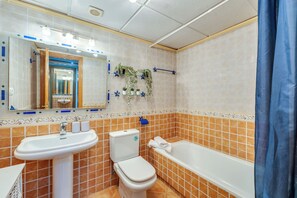 A bathroom with a sink, toilet, and bathtub, tiled in orange and white, with a mirror and decorative plants. - LXR Coloso, 2-bedroom apartment with an ocean view. (Benalmádena)