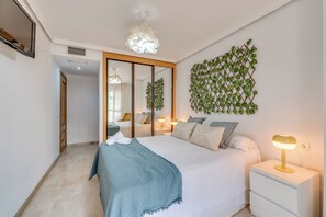 A bedroom with a bed, bedside tables, a mirror, and a wall-mounted plant. - LXR Coloso, 2-bedroom apartment with an ocean view. (Benalmádena)