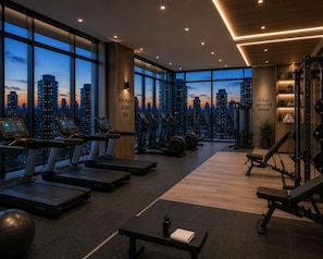 Ett gym med löpband, crosstrainers och utrustning för styrketräning, stora fönster med utsikt över staden och inspirerande texter på väggarna.