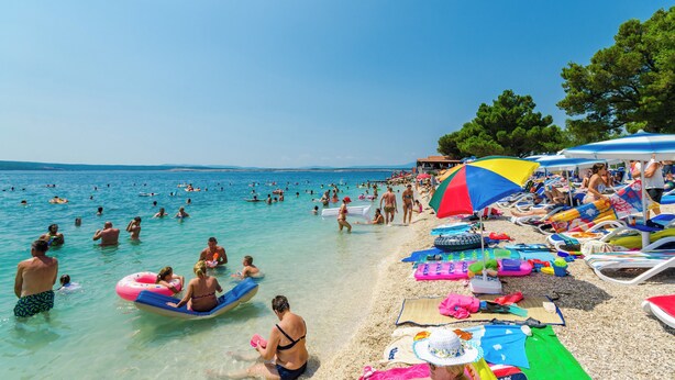 Ein Strand mit badenden und sonnenden Personen, Sonnenschirmen und Liegestühlen.