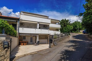 Ein zweistöckiges Gebäude mit einem Balkon, einer Steinmauer und einem gepflasterten Auffahrtsweg.