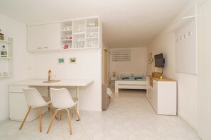 Ein kleines Zimmer mit einem Bett, einem Schreibtisch mit Stühlen, einem Fernseher und einem weißen Schrank mit Regalen.