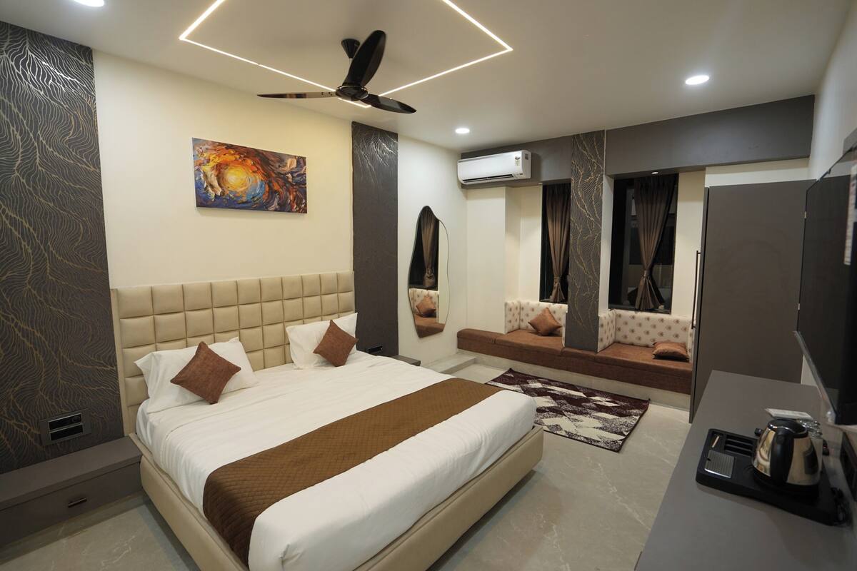 Una habitación de hotel moderna con una cama grande, ventilador de techo, equipo de aire acondicionado, zona de estar y televisor.