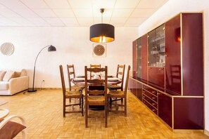 Ein Essbereich mit rundem Tisch, Holzstühlen, einer schwarzen Pendelleuchte, einer Couch und einem Schrank mit Glastüren.