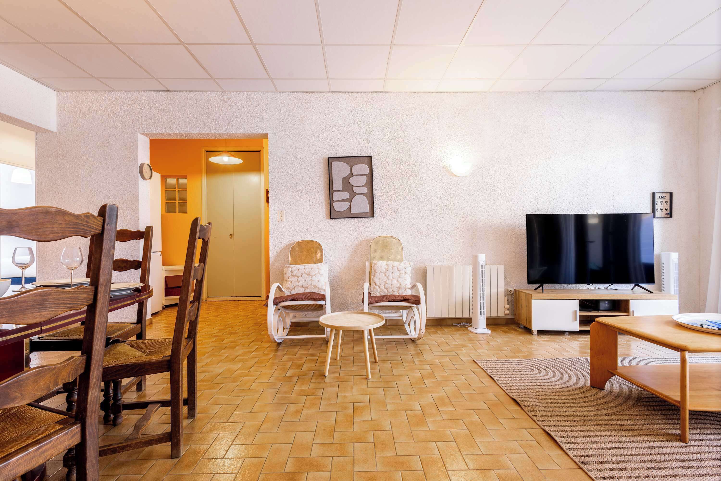 Ein Wohnzimmer mit einem Holzessttisch, zwei Stühlen, einem kleinen runden Tisch, einem Flachbildfernseher und einer Heizung.