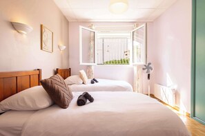 Ein Hotelzimmer mit zwei Betten, einem Fenster mit Blick, einem Deckenventilator und Wandleuchten.